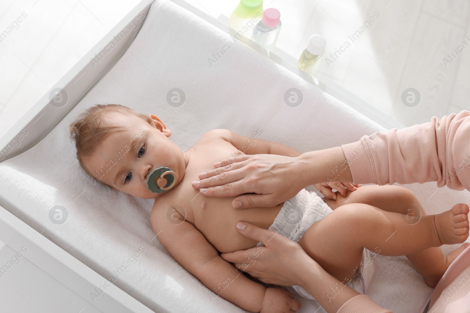 Photo of Mother massaging her cute baby with oil on changing table at home, closeup
