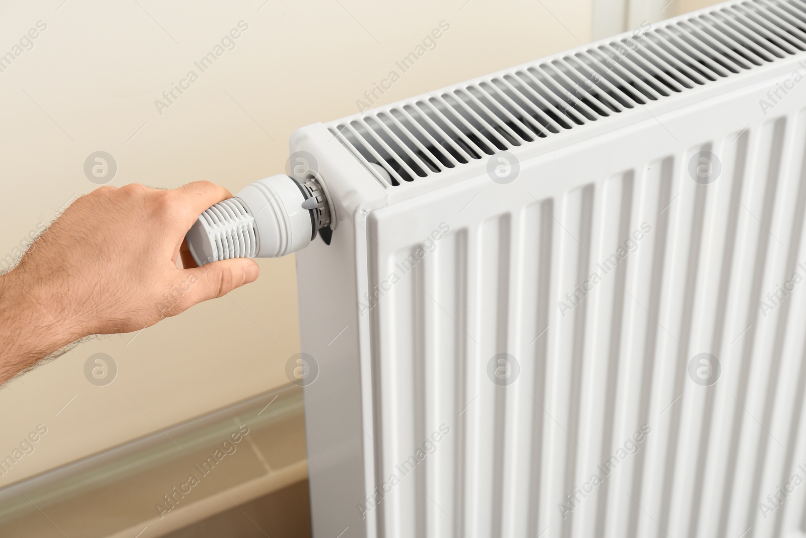 Photo of Man adjusting heating radiator thermostat indoors