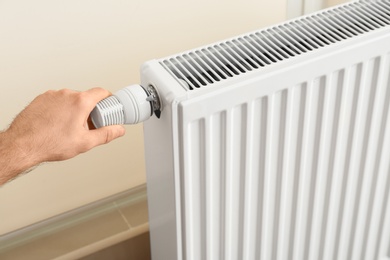 Man adjusting heating radiator thermostat indoors