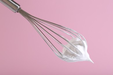 Whisk with whipped cream on pink background