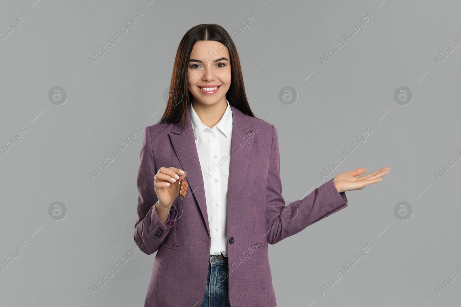 Photo of Female real estate agent holding key on grey background