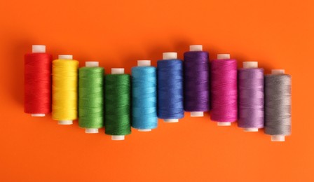 Photo of Different colorful sewing threads on orange background, flat lay