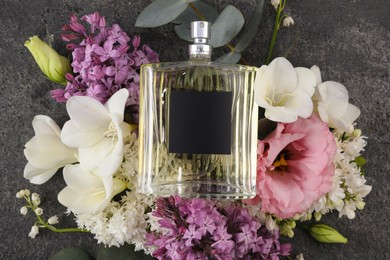 Photo of Bottle of luxury perfume and floral decor on dark grey table, top view