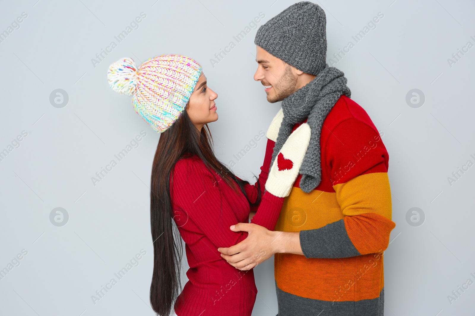 Photo of Young happy couple in warm clothes on light background. Christmas celebration