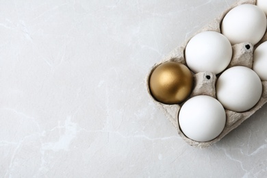 Photo of Carton with golden egg and others on light background, top view