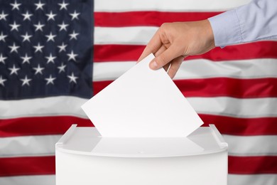 Image of Man putting his vote into ballot box against national flag of United States, closeup