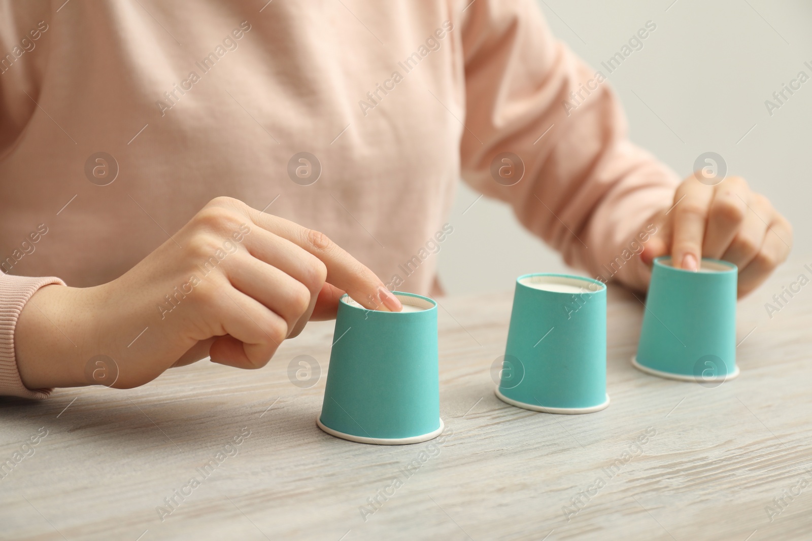 Photo of Woman playing shell game with turquoise cups at wooden table, closeup