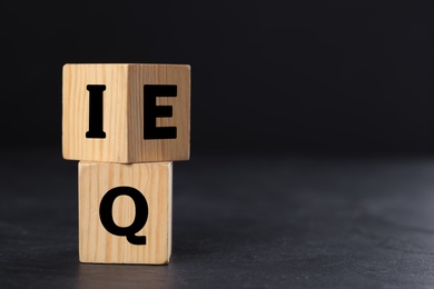 Photo of Wooden cubes with letters E, I and Q on black slate table. Space for text