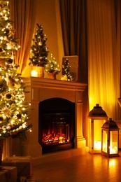 Photo of Beautiful fireplace, Christmas tree and other decorations in living room at night. Interior design