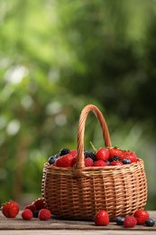 Photo of Wicker basket with different fresh ripe berries on wooden table outdoors