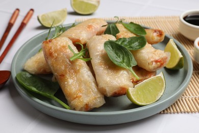 Photo of Plate with tasty fried spring rolls, spinach, arugula and lime on white table, closeup