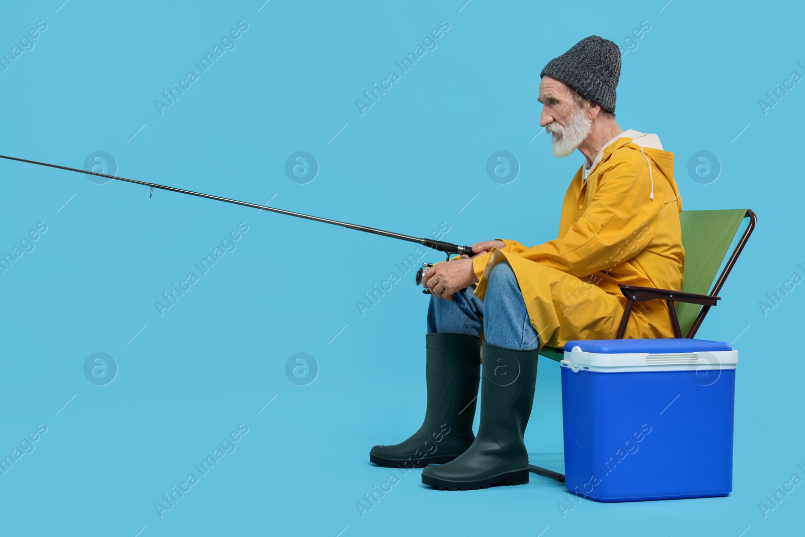 Photo of Fisherman with rod and cool box on chair against light blue background