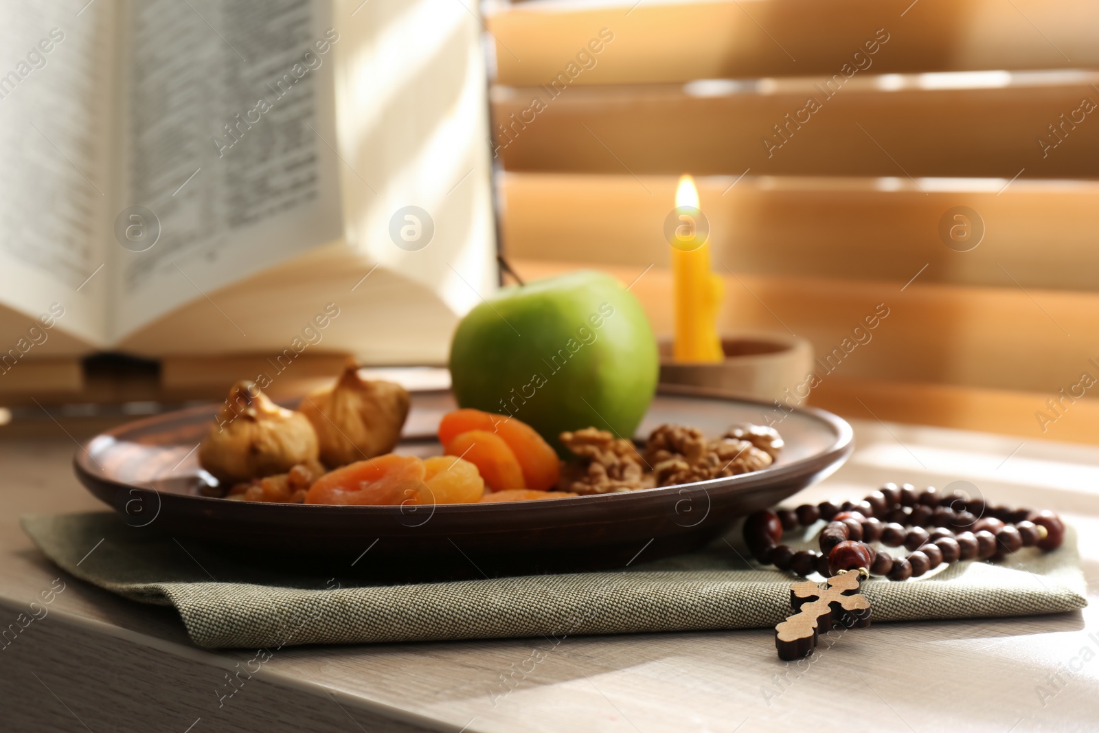 Photo of Dried fruits, apple, prayer beads, Bible and candle on window sill indoors. Great Lent season