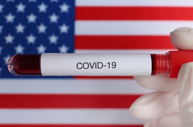 Photo of Scientist holding test tube with blood sample over American flag, closeup. Coronavirus pandemic in USA