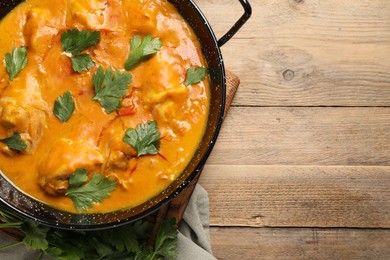 Photo of Tasty chicken curry with parsley on wooden table, top view. Space for text