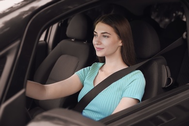 Young woman with fastened safety belt on driver's seat in car