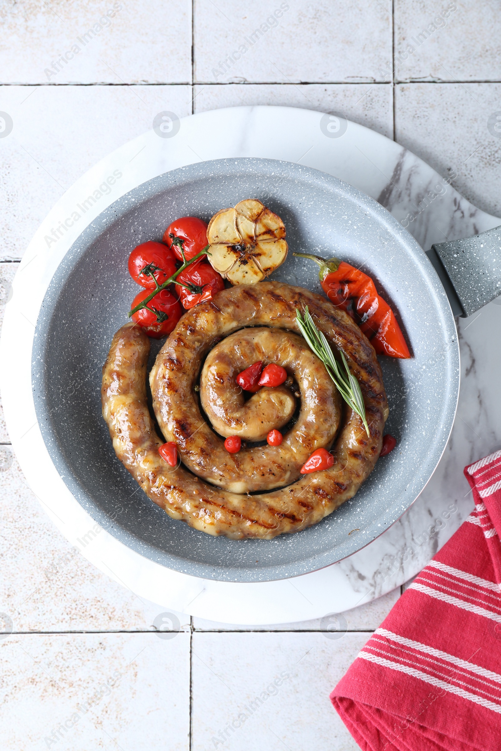 Photo of Delicious homemade sausage with garlic, tomatoes, rosemary and chili in frying pan on light tiled table, top view