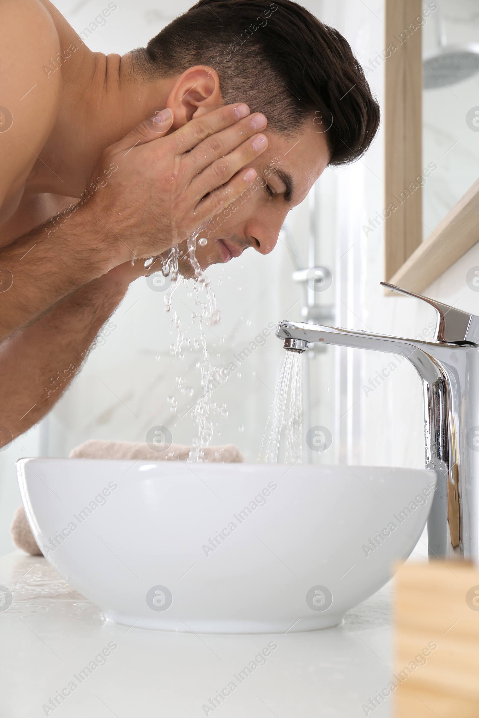 Photo of Handsome man washing face over sink in bathroom