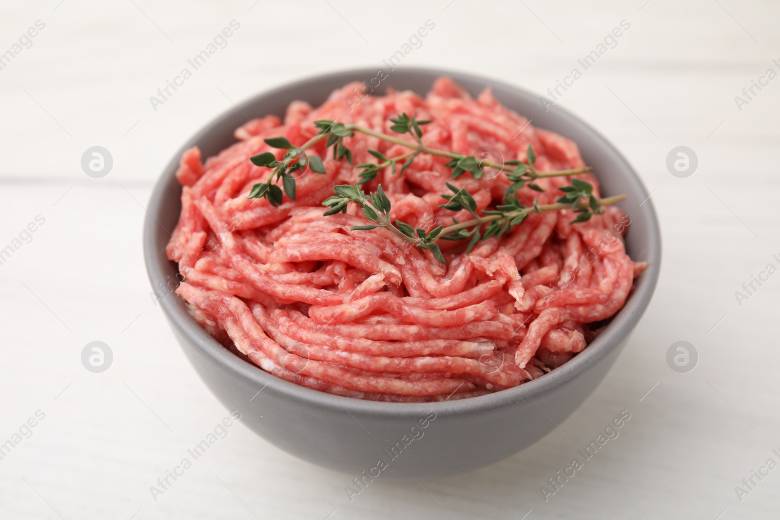 Photo of Fresh raw ground meat and thyme in bowl on white table, closeup