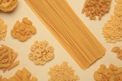 Photo of Different types of pasta on beige background, flat lay