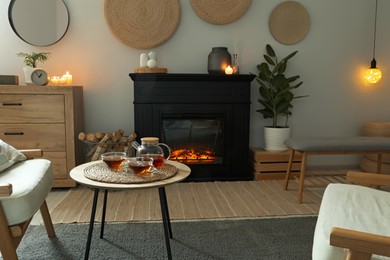 Stylish fireplace near coffee table with tea in cosy living room. Interior design