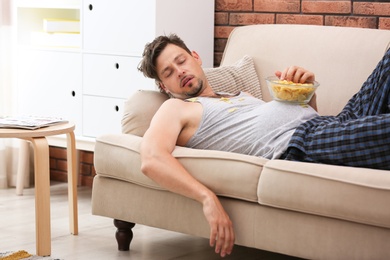Photo of Lazy man with bowl of chips sleeping on sofa at home