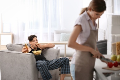 Photo of Lazy husband watching TV and his wife cooking at home
