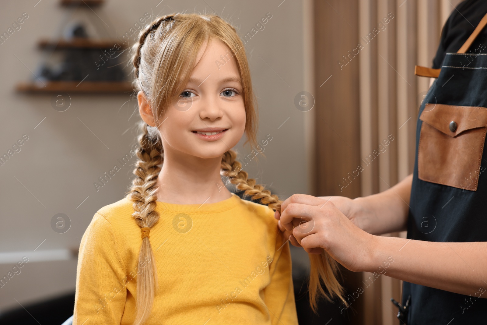 Photo of Professional hairdresser braiding girl's hair in beauty salon