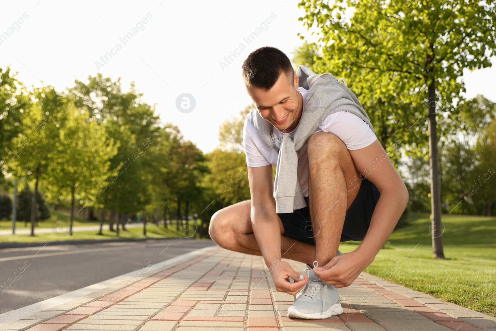 Photo of Young man tying laces of sneakers outdoors. Morning fitness