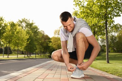 Photo of Young man tying laces of sneakers outdoors. Morning fitness