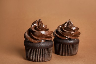 Delicious chocolate cupcakes with cream on brown background