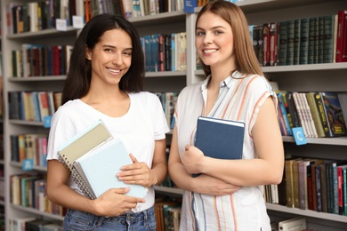 Young women with books near shelves in library