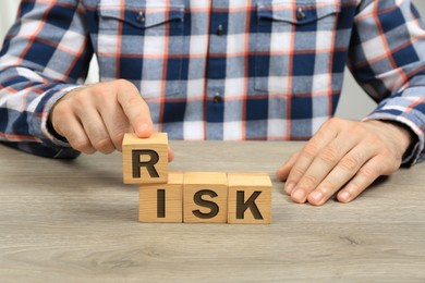 Photo of Man making word Risk of cubes at wooden table, closeup