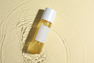 Bottle of cosmetic oil in water on beige background, top view