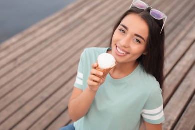 Happy young woman with delicious ice cream in waffle cone outdoors. Space for text