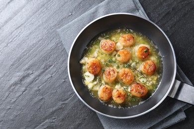 Delicious scallops with sauce in frying pan on dark gray textured table, top view. Space for text