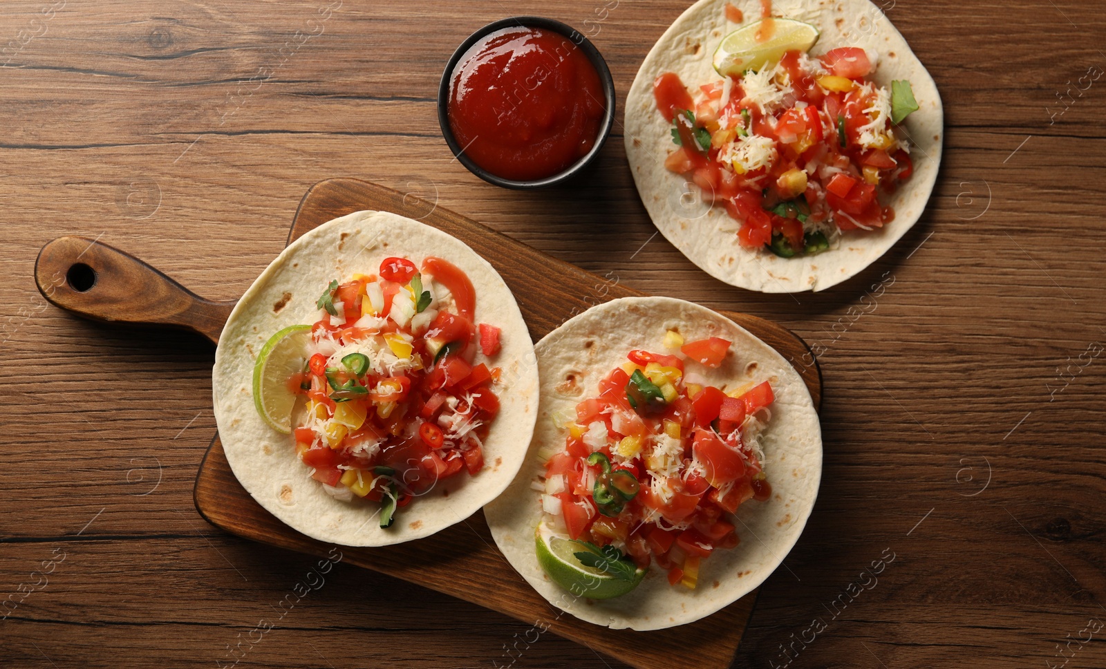 Photo of Delicious tacos with vegetables, lime and ketchup on wooden table, flat lay