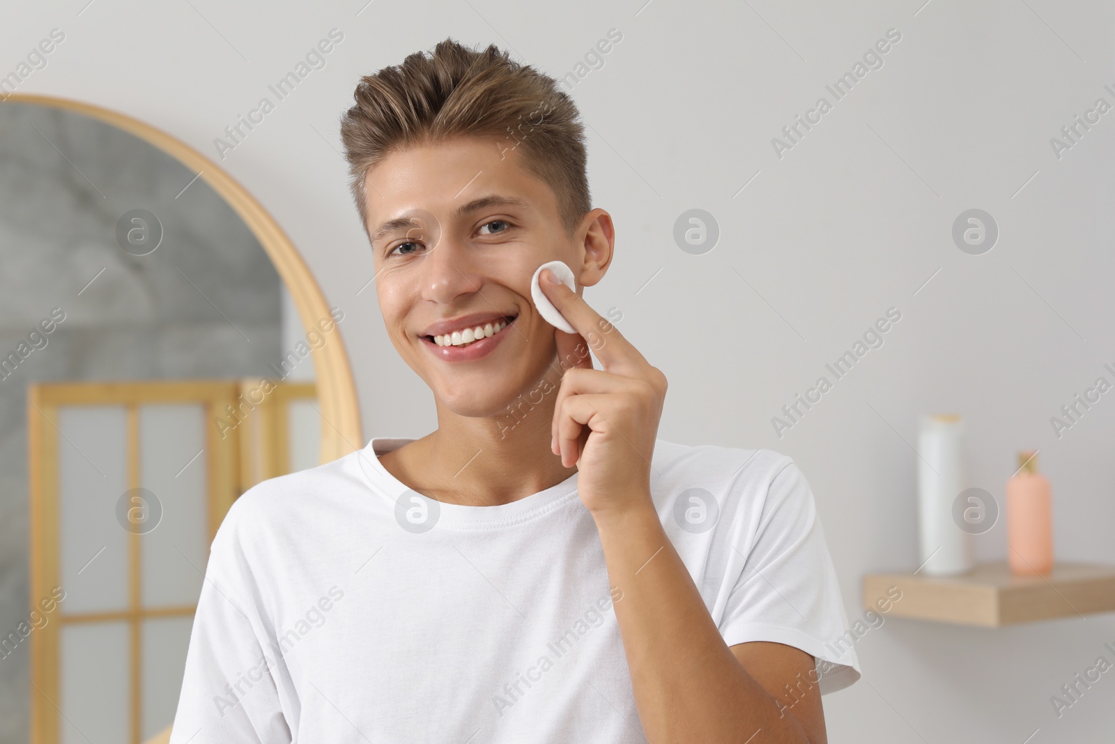 Photo of Handsome young man cleaning face with cotton pad in bathroom