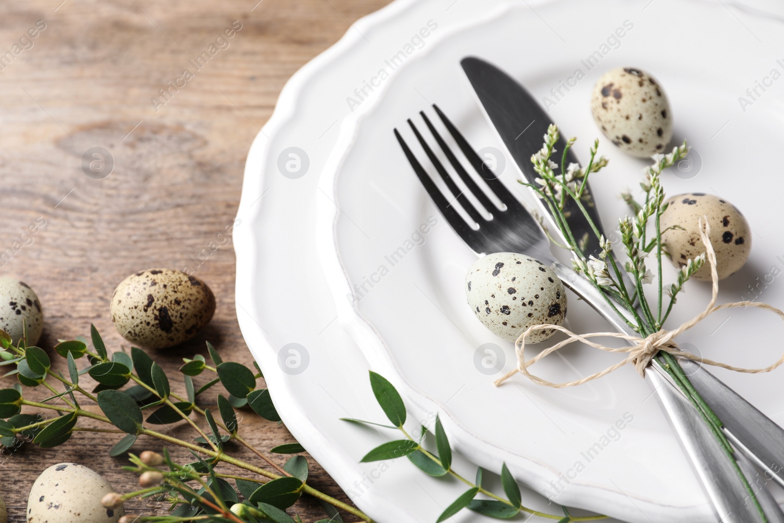 Photo of Festive Easter table setting with quail eggs and floral decor on wooden background, closeup