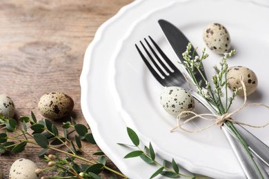 Festive Easter table setting with quail eggs and floral decor on wooden background, closeup