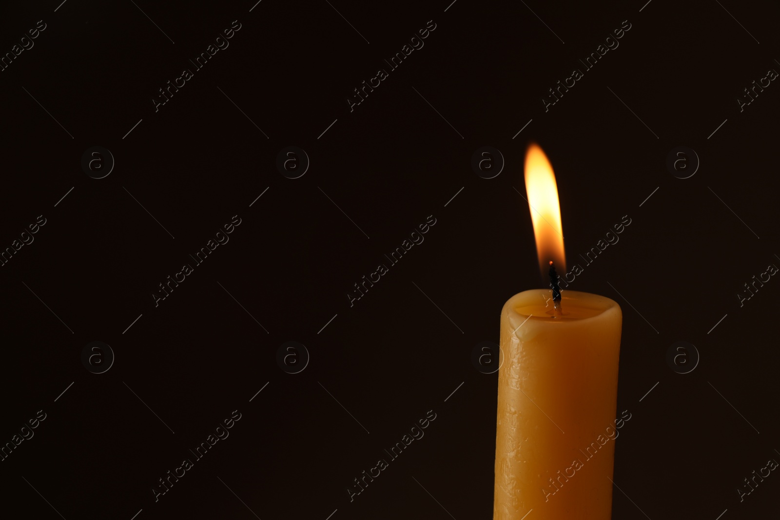 Photo of Burning church wax candle on dark background, space for text