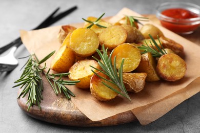 Photo of Tasty baked potato and aromatic rosemary served on wooden board, closeup