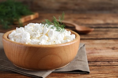 Fresh cottage cheese with dill in bowl on wooden table, closeup