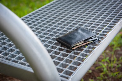 Photo of Black wallet on metal bench outdoors. Lost and found