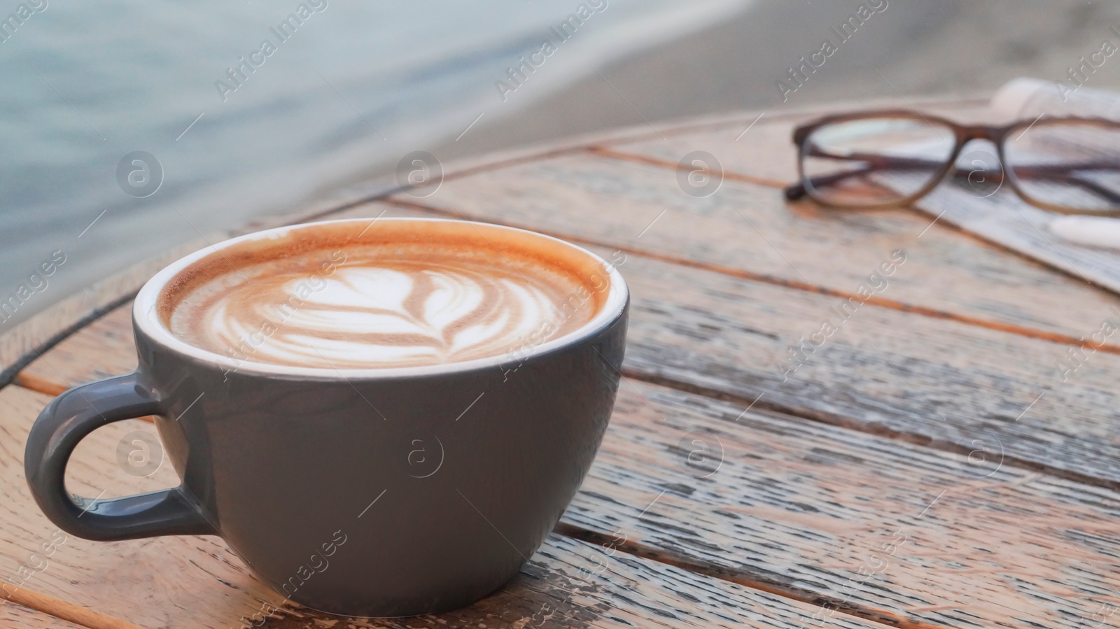 Photo of Cup of delicious coffee, eyeglasses and newspaper on wooden table, closeup. Space for text