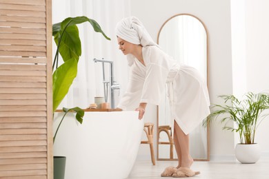 Photo of Beautiful woman in white robe near tub in light bathroom