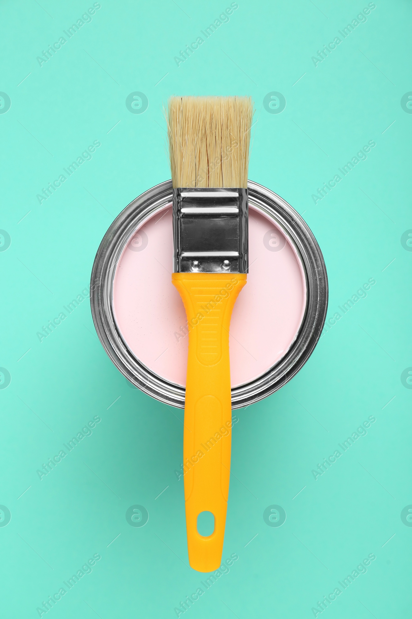 Photo of Can of pink paint with brush on turquoise background, top view