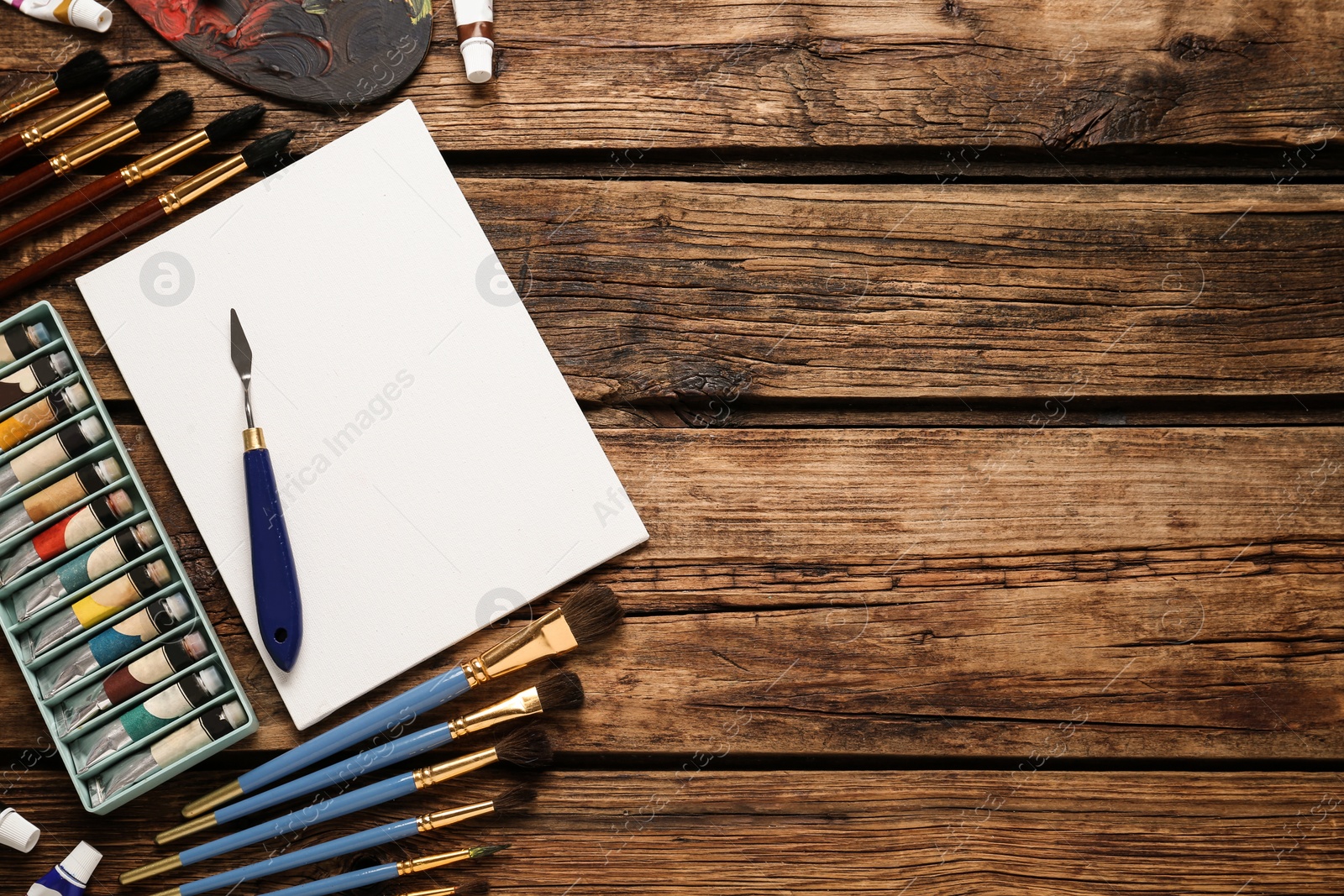 Photo of Blank canvas, brushes and paints on wooden table, flat lay. Space for text