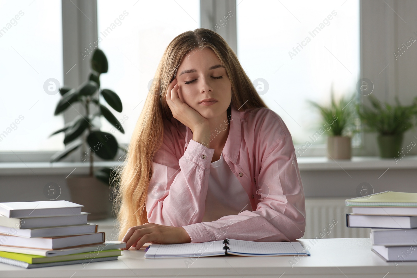 Photo of Young tired woman sleeping near books at white table indoors