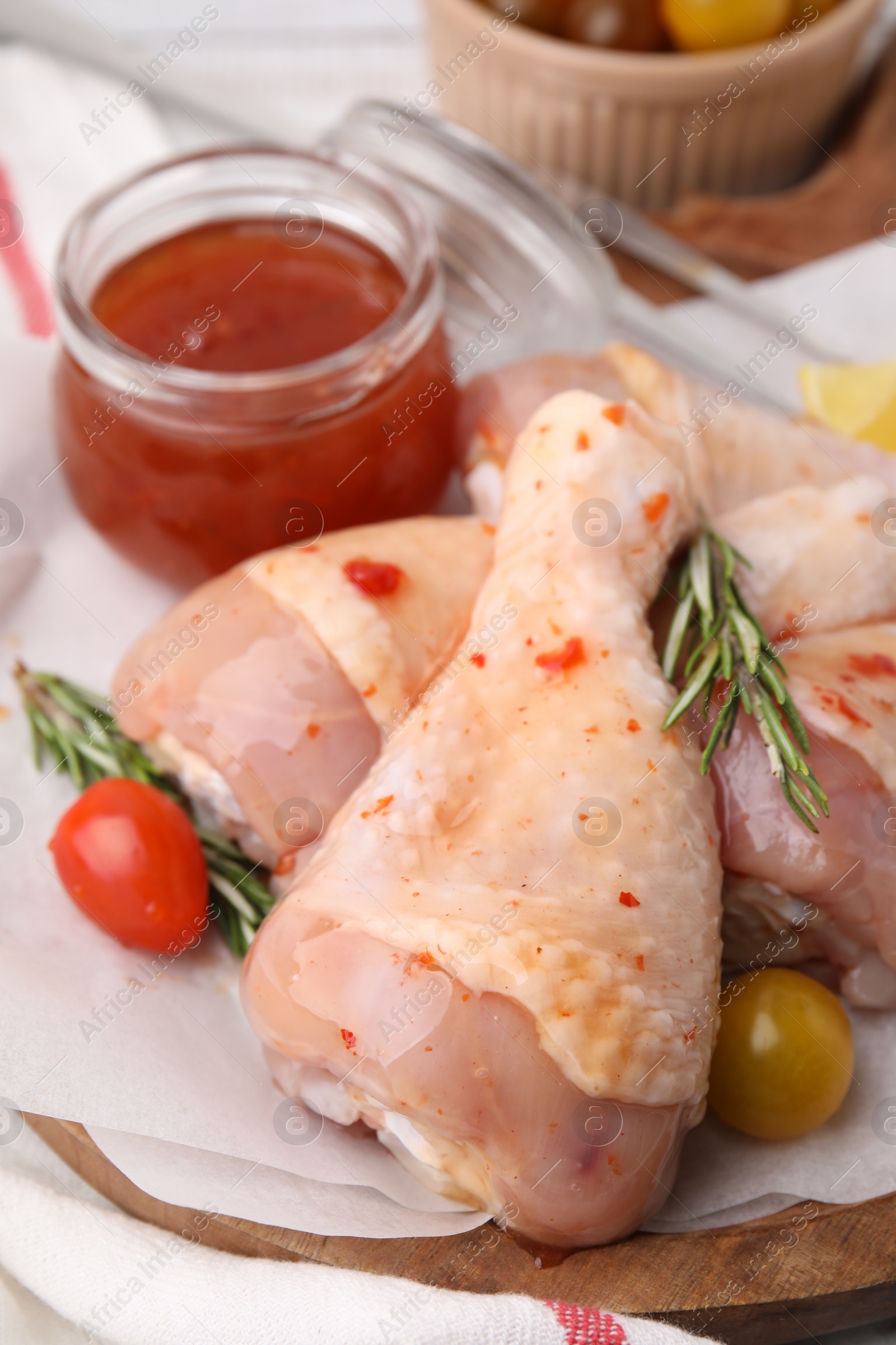 Photo of Marinade, raw chicken drumsticks, rosemary and tomatoes on table, closeup